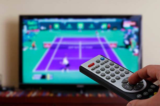 Watching a tennis match in the television, with a tv remote control in the hand